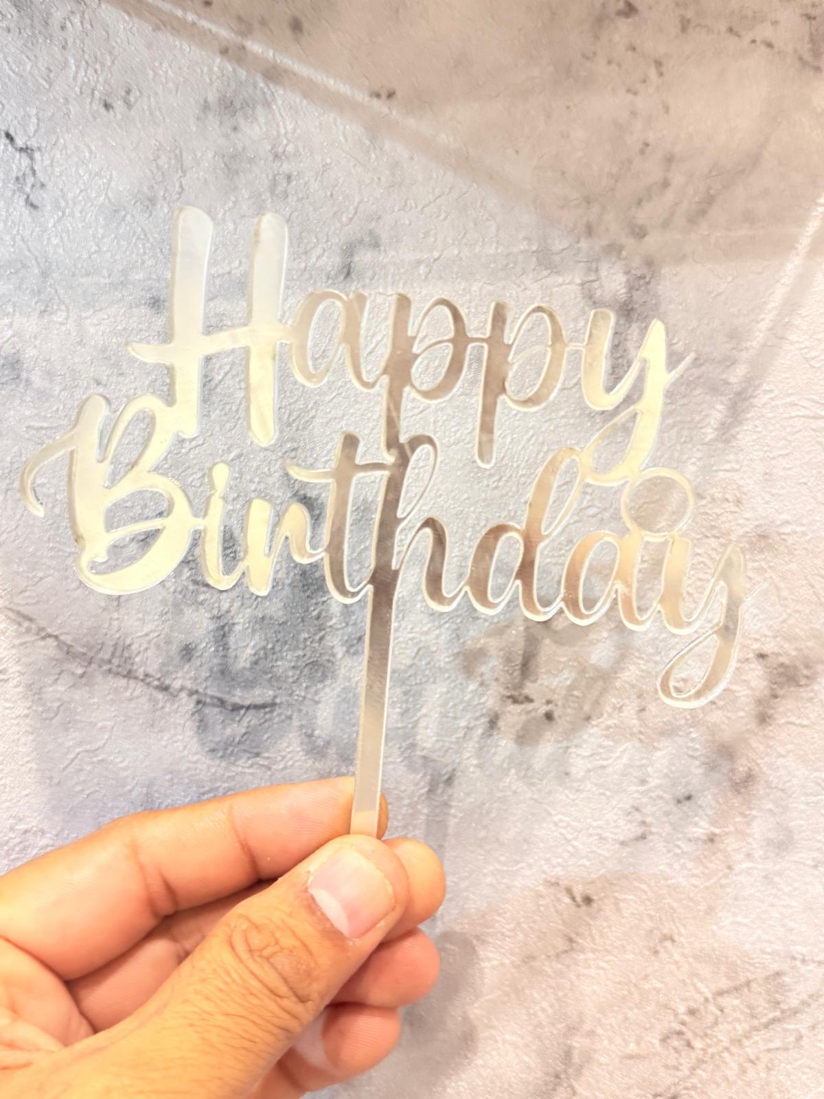Clear acrylic Happy Birthday cake topper with "Happy Birthday" text, designed by Ward and Haneen for celebratory cakes.