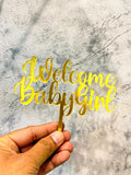 Gold Welcome Baby Girl cake topper by Ward and Haneen, featuring elegant lettering for baby shower celebrations.
