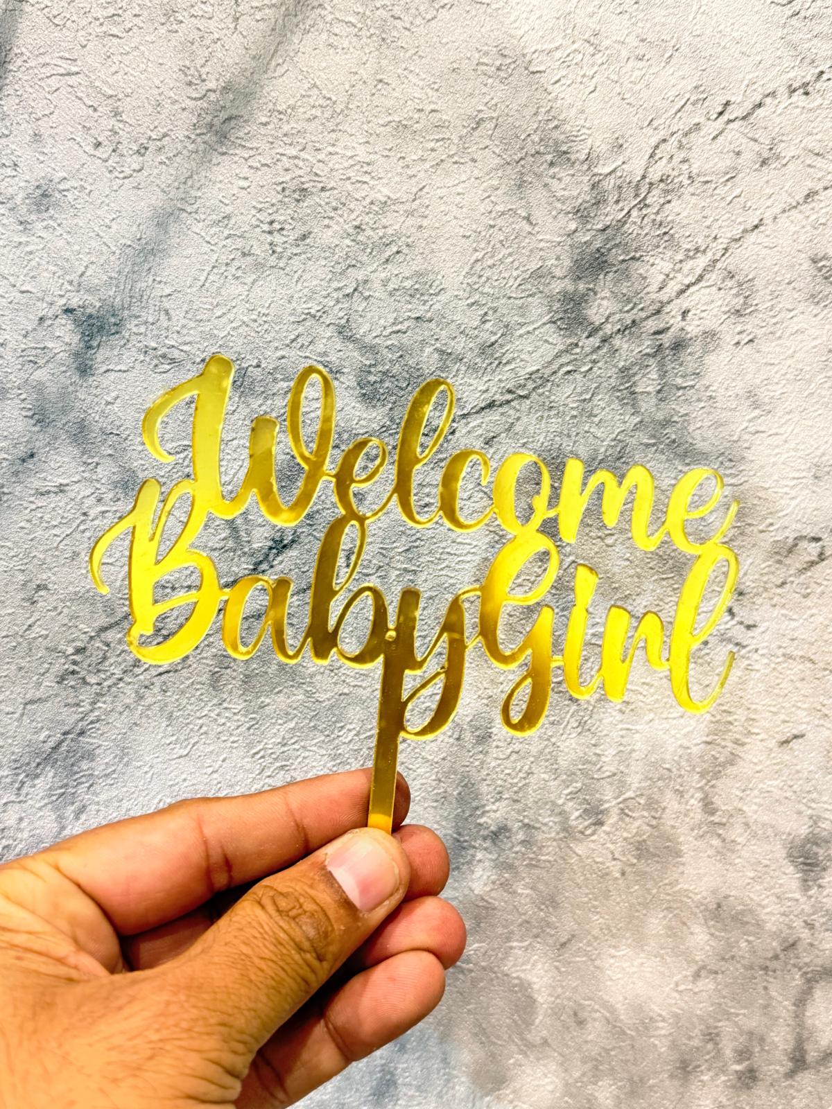 Gold Welcome Baby Girl cake topper by Ward and Haneen, featuring elegant lettering for baby shower celebrations.