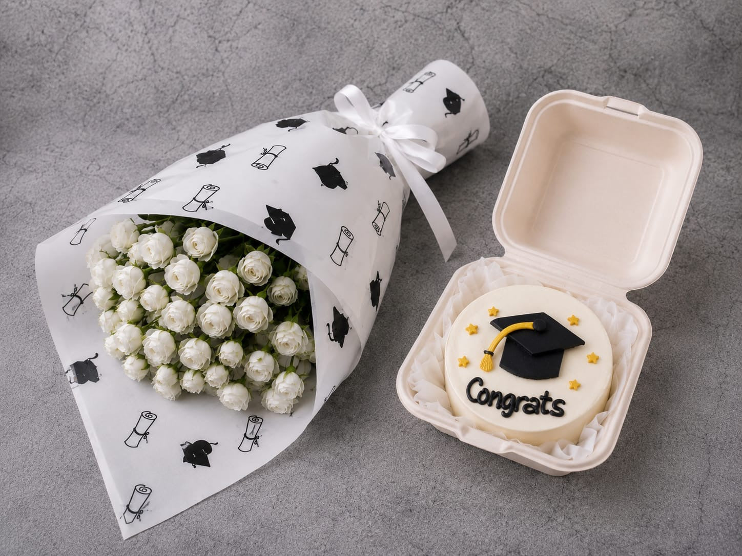 Graduation gift set from Ward and Haneen featuring white roses and a decorated bento cake on a wooden table.