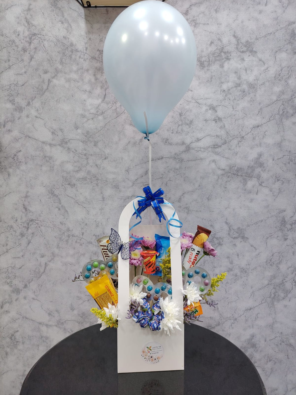 Blue balloon and chocolate gift basket by Ward and Haneen, featuring assorted chocolates and decorative blue balloons.