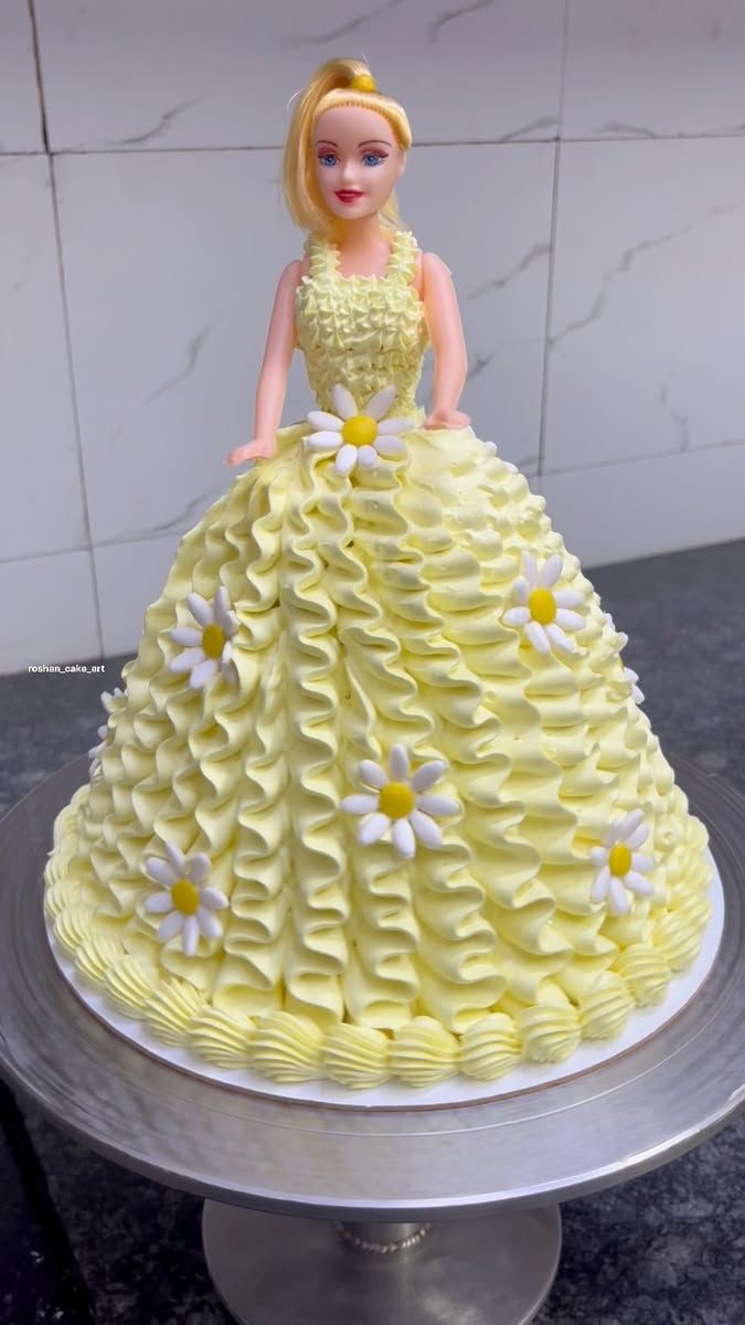 Yellow cake designed to resemble a doll with floral decorations on a marble surface.